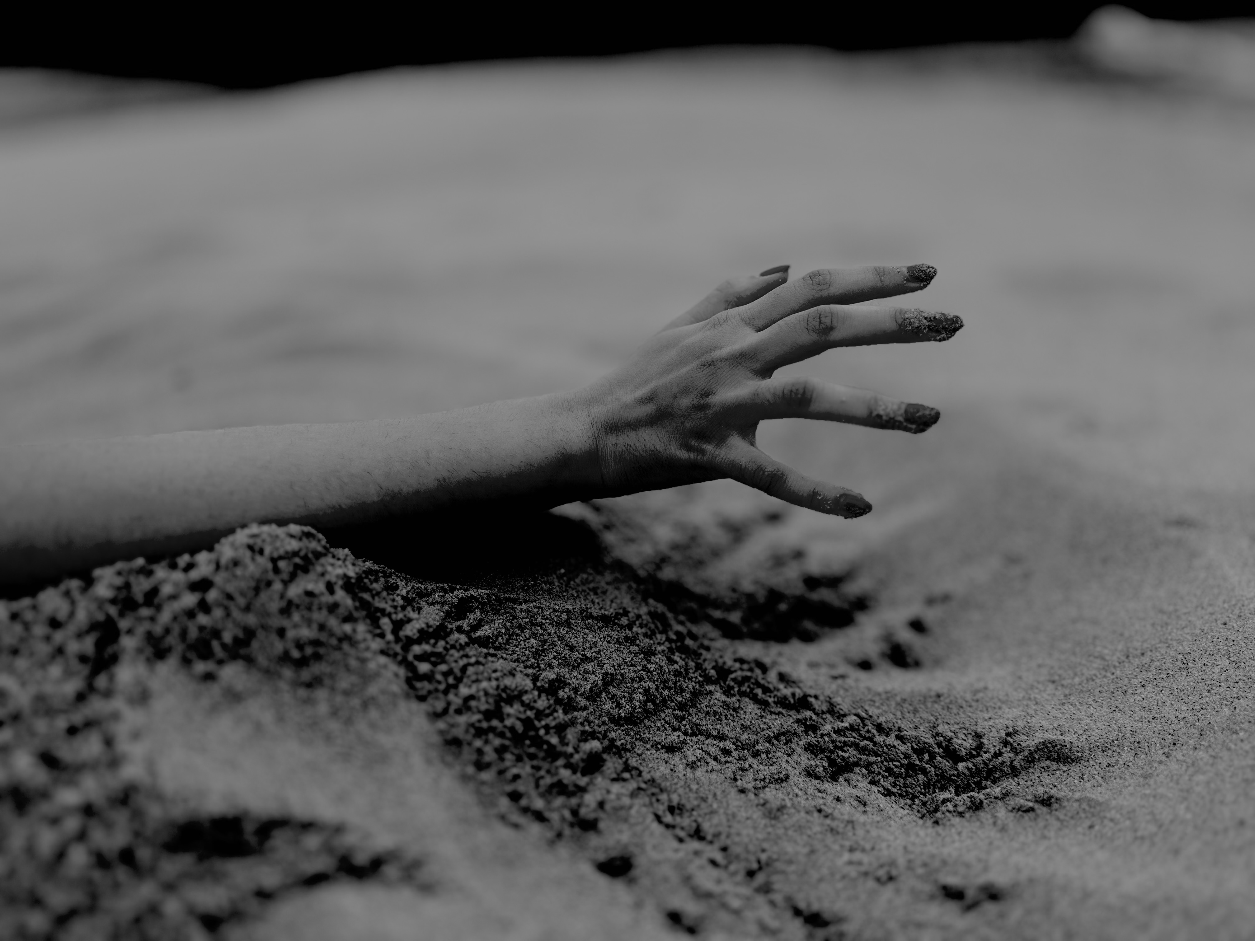 a black and white photo of a hand reaching out over a sandy beach