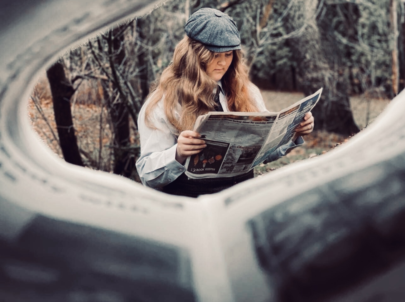 camera looking through newspaper at woman reading newspaper