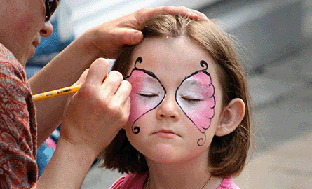 Girl with brown hair getting a pink butterfly painted on her face.