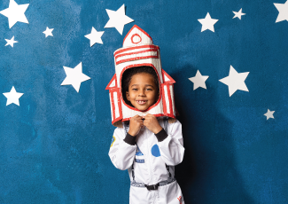 child dressed in as an astronaut standing in front of a blue background with stars