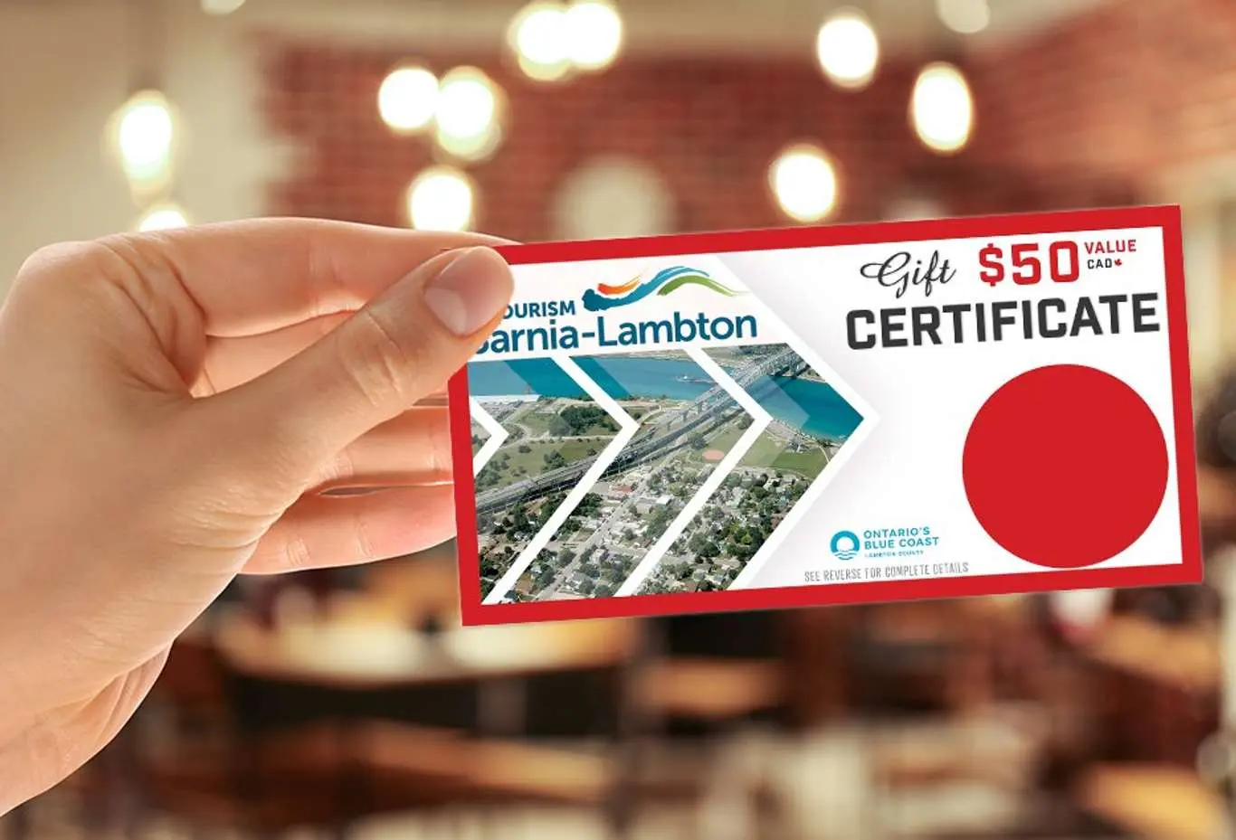 A hand holding out a Tourism Sarnia-Lambton gift certificate