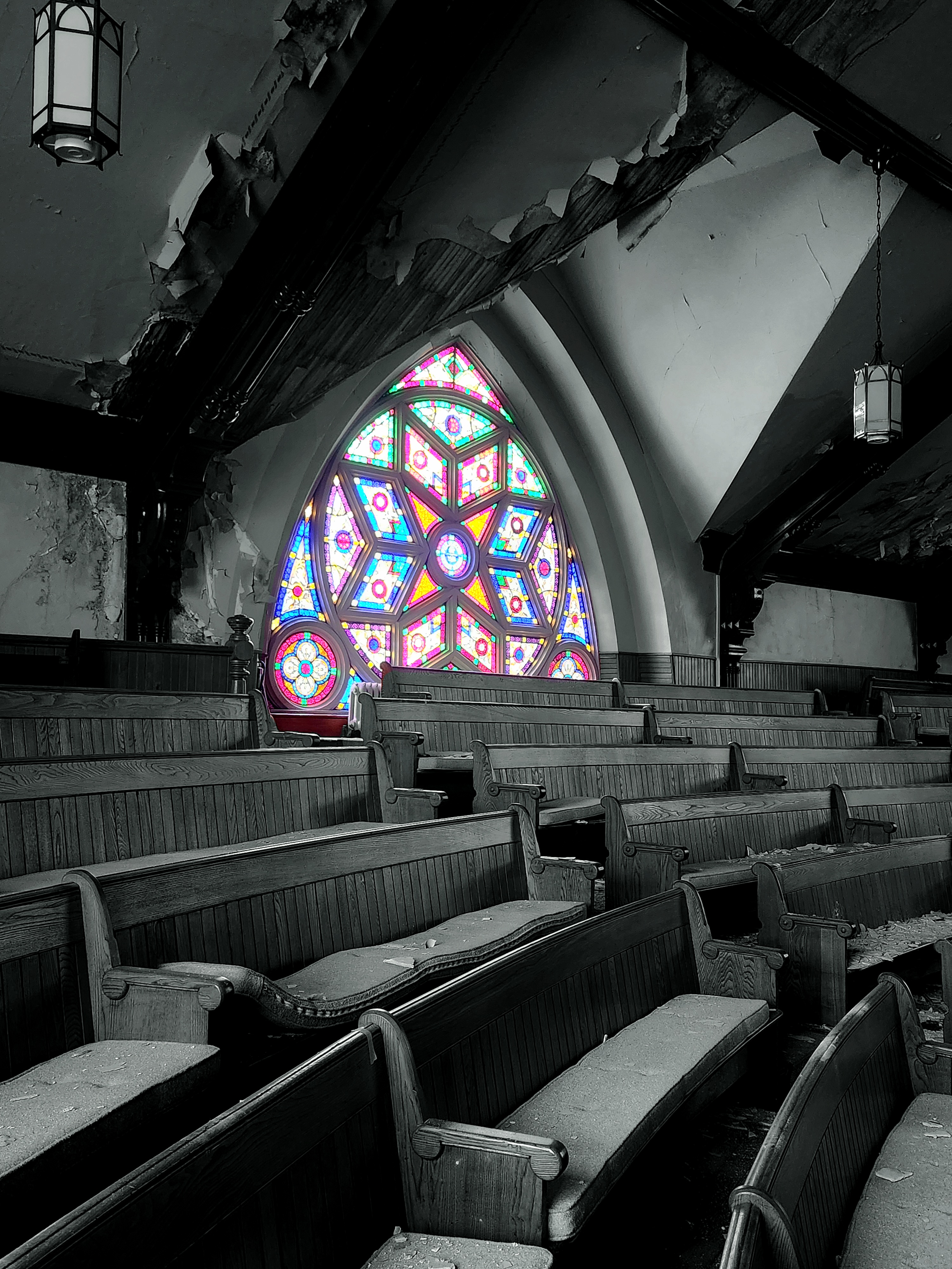 a black and white photo of a ruined church with a colourful stain glass window